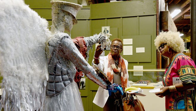 Pat Wade and Jackie Benjamin of Paterson, L-R, admire an outfit "Boots On The Ground To Cyber" designed by Victoria Pero during the opening reception of the Paterson Eco-Chic exhibit at the Paterson Museum Sunday, September 17, 2017. The outfit is made from Desert Storm camouflage, plastic sheeting, newspaper print and other recycled materials.